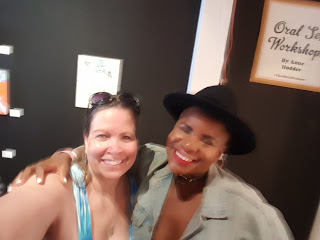 Smiling white woman with sunglasses on top of her head next to smiling young Black woman wearing red lipstick and a black hat