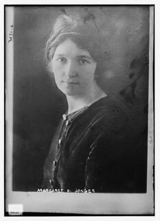 Photograph of Margaret Sanger, a pale-skinned woman in a hat with dark hair, looking directly at the camera